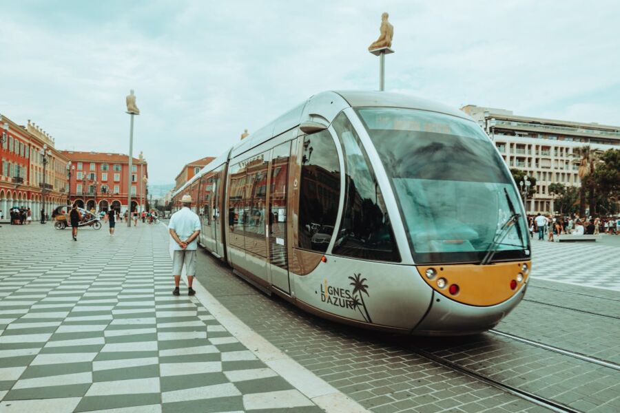 Modern tram in Nice square with pedestrians, historic architecture, and Mediterranean ambiance.