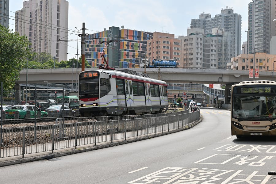Urban scene with modern tram, bus, diverse architecture, and vibrant city life.