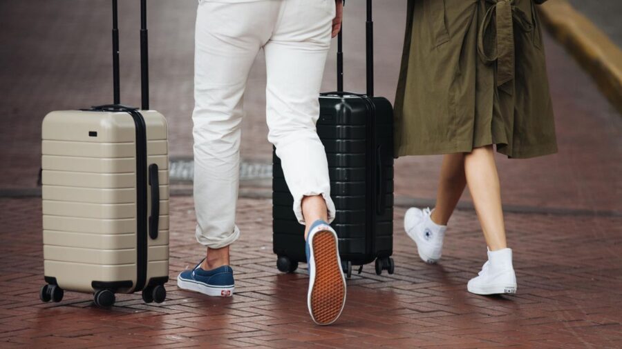 Urban couple traveling with stylish suitcases on brick sidewalk in daytime.