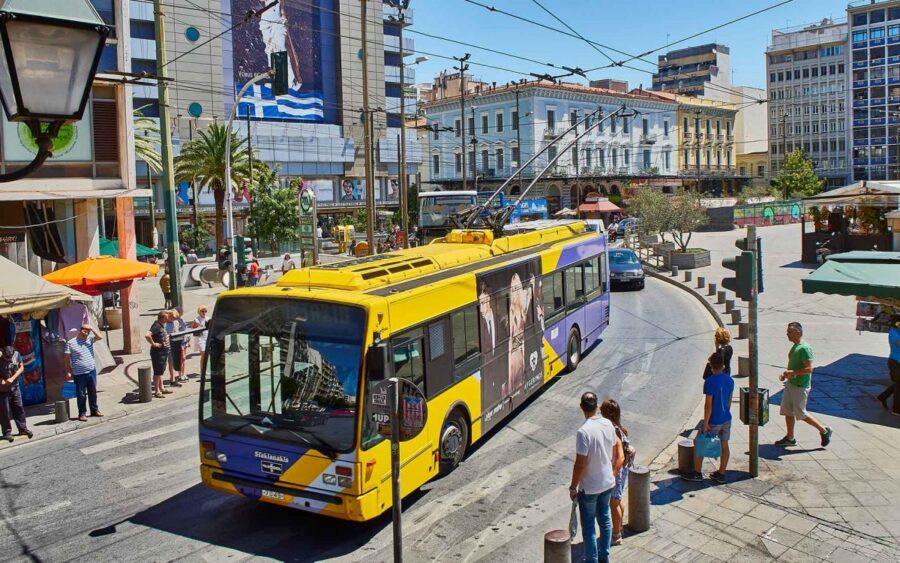 Vibrant city scene with trolleybus, pedestrians, diverse architecture, and lively urban activities.