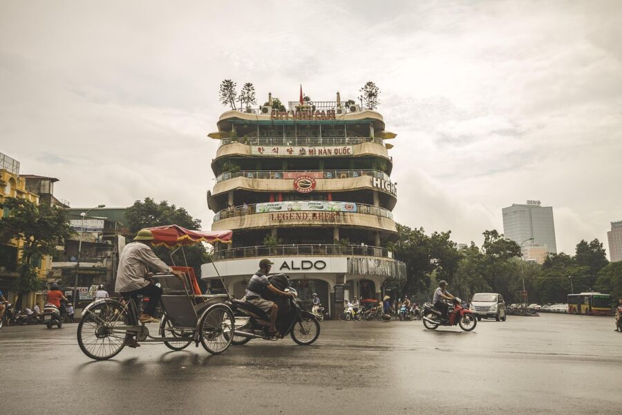 Bustling Vietnamese cityscape with modern architecture, traditional transport, multicultural signage, and greenery.