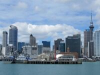 Coastal city skyline with skyscrapers, waterfront, boats; vibrant urban landscape against a bright sky.