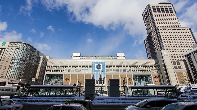 Sapporo Station winter cityscape with snow, modern buildings, traffic, and glass bus shelters.