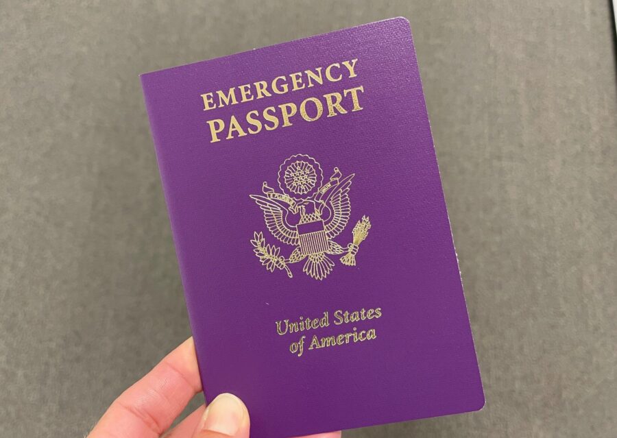 Emergency US passport in hand, displaying purple cover and gold eagle emblem.