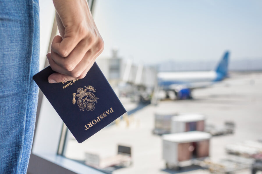 Close-up of a hand holding a USA passport at an airport, ready for travel.