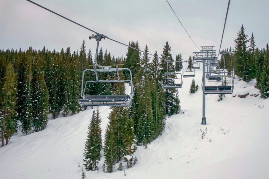Ski lift at a Vail, Colorado resort, surrounded by lush green trees under a clear blue sky