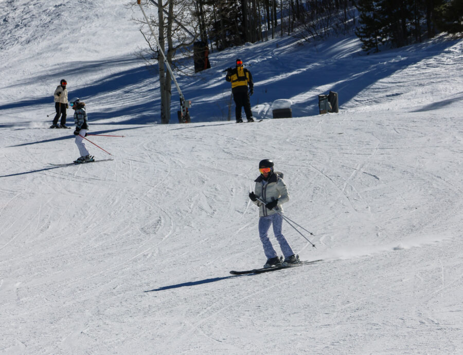Skiers glide down sunlit slopes in Vail, Colorado, surrounded by the majestic Rocky Mountains during a late afternoon