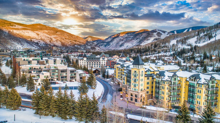 Aerial panorama of Vail, Colorado, showcasing the village skyline and surrounding mountains in a clear blue sky