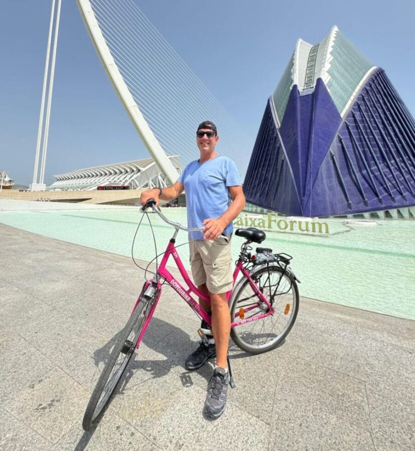 Man next to his bike in front of a building, part of the Valencia City Highlights Guided Bike Tour experience.