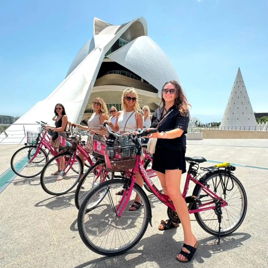 Women cyclists pose in front of a building, showcasing the Valencia City Highlights Guided Bike Tour experience.