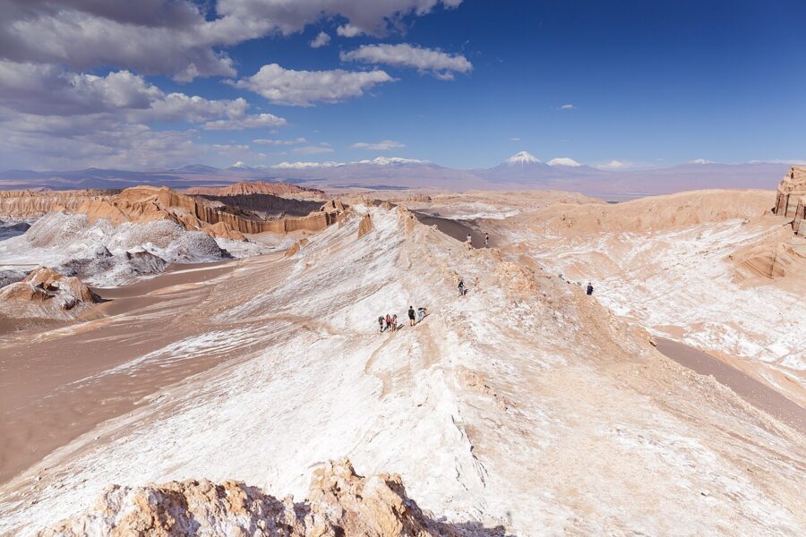 People walking on a mountain trail in the desert landscape of Valle de la Luna, Chile, with panoramic views.