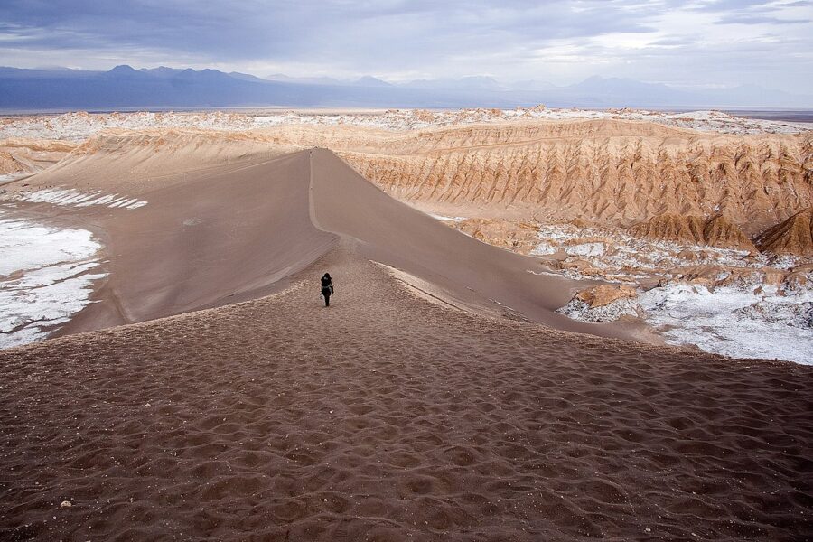 Person walking up a sand dune in the Valle de la Luna desert, showcasing the vast, arid landscape.