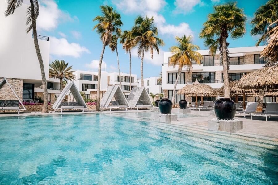The pool at Van der Valk Plaza Beach & Dive Resort, surrounded by palm trees and lounge chairs in Bonaire