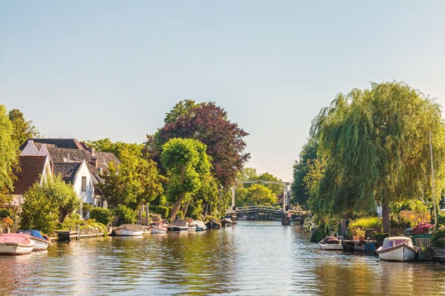 The Vecht River panorama features boats on a canal surrounded by lush trees in the heart of a town.