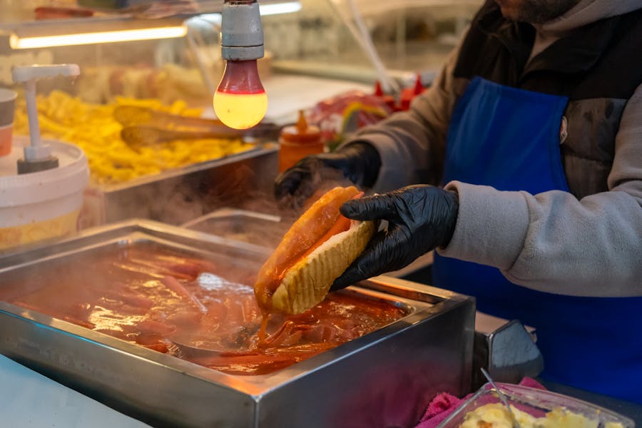 Vendor in Istanbul prepares steaming hot dog with spicy sauce and condiments.