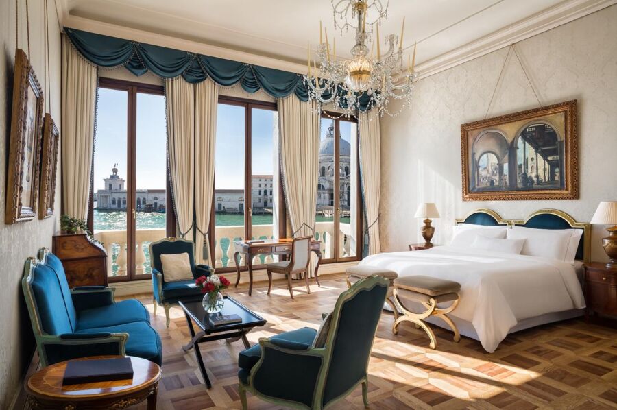 Luxurious Venetian hotel room with king-size bed, chandeliers, and canal view.