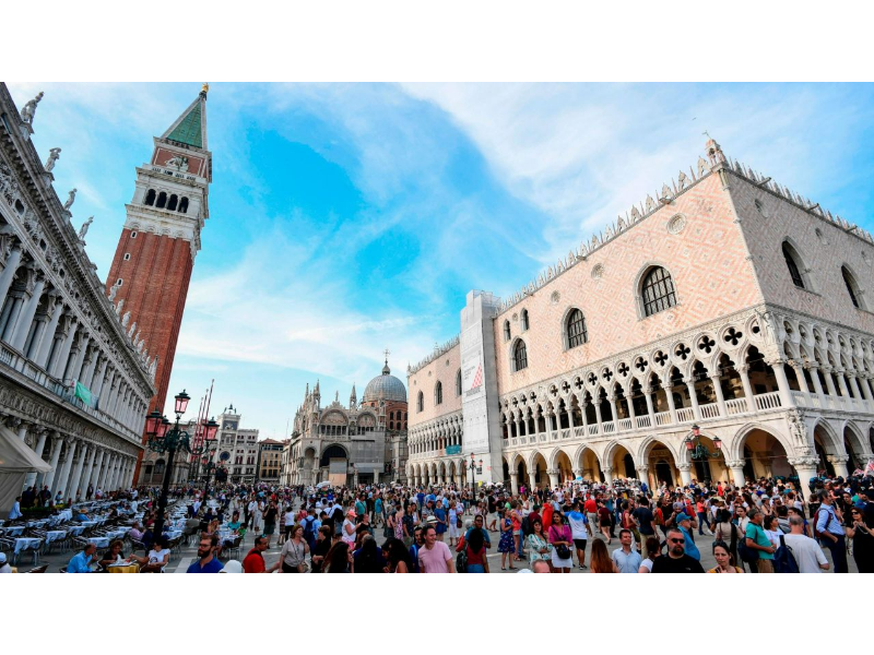 Vibrant Saint Marks Square in Venice, bustling with tourists, historic architecture, blue sky.
