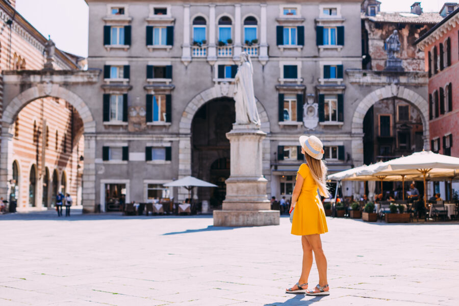 Tourists in a yellow dress and wide-brimmed hat explore the vibrant square in Verona, Italy, wearing comfortable footwear