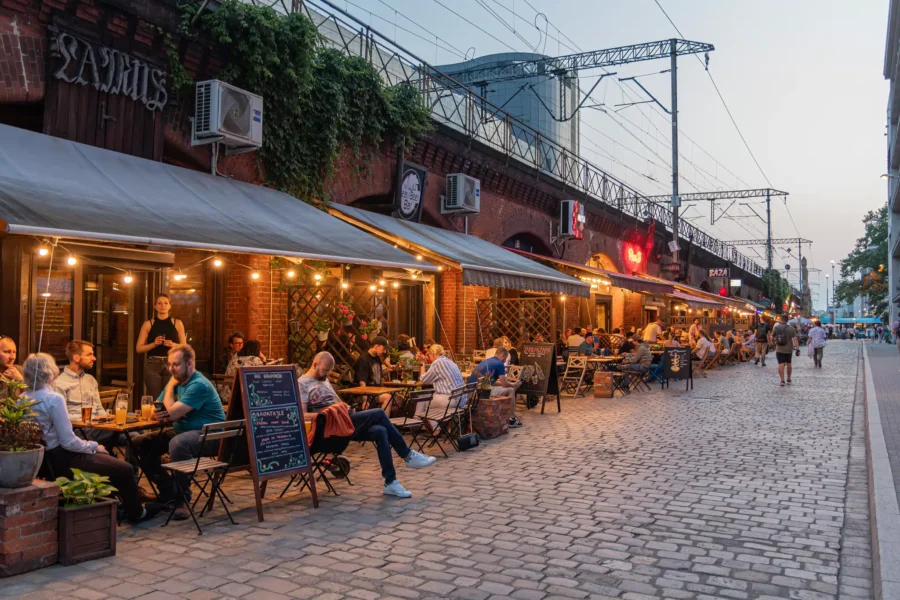 Wroclaw viaduct restaurants and sidewalk cafes on cobblestone street with outdoor terraces and string lights.