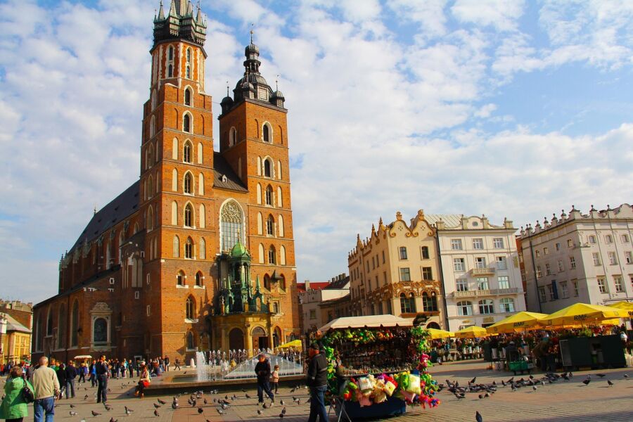 St. Mary’s Basilica in bustling square with Gothic architecture, people, pigeons, cafes, and vendors.