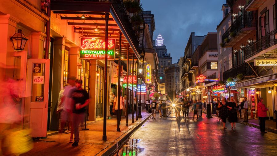 Lively New Orleans street scene at twilight with neon lights and diverse crowd.