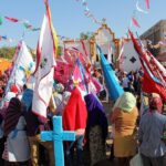 Cultural festival with diverse crowd in traditional clothing, flags, and decorated religious building.