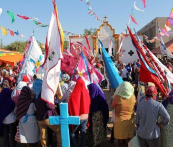 Cultural festival with diverse crowd in traditional clothing, flags, and decorated religious building.