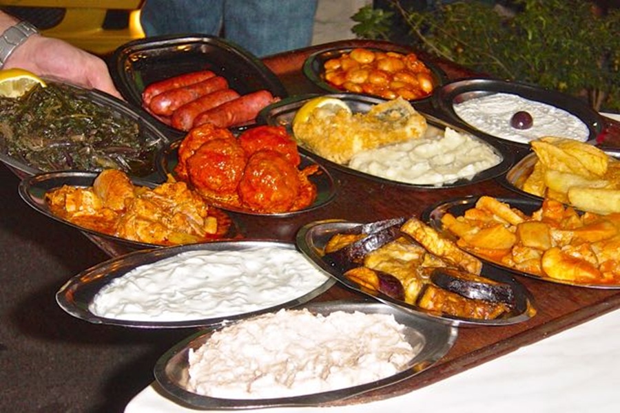 Vibrant Mediterranean feast with meats, sides, and dips in a communal outdoor setting.