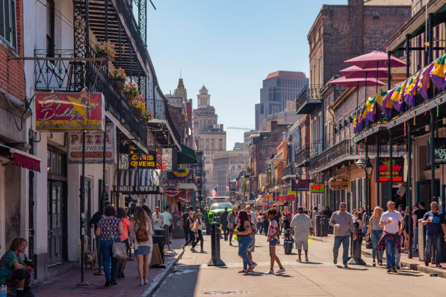Lively New Orleans French Quarter street scene with people, colorful signs, and historic architecture.