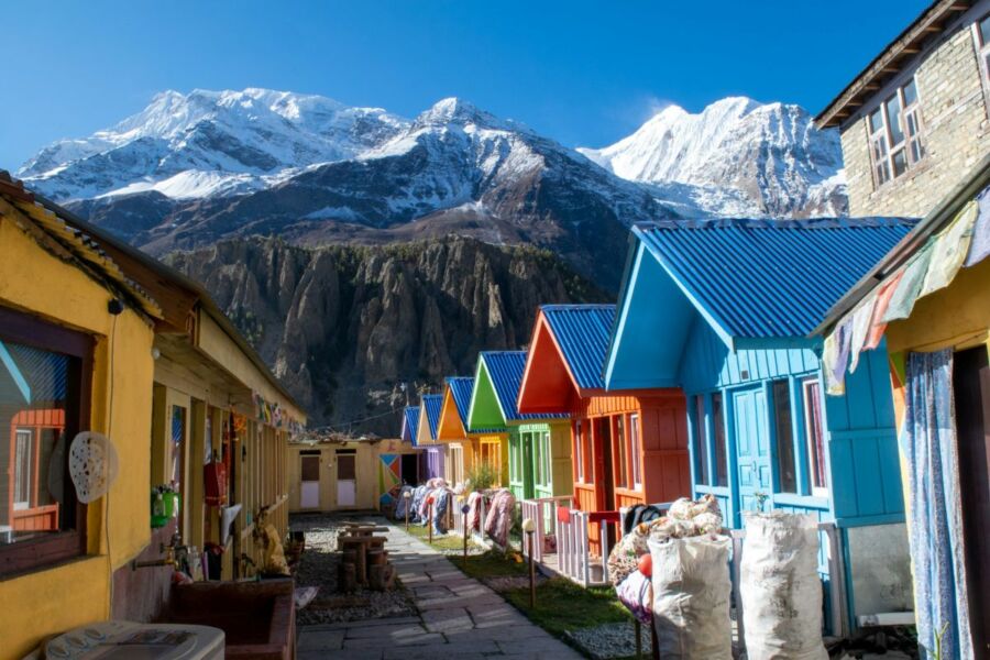 Colorful mountain village with cottages and snow-capped peaks under blue sky.