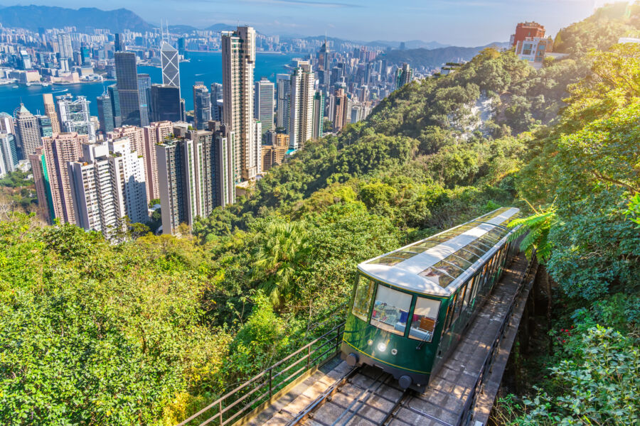 The iconic green tram climbs the steep slope of Victoria Peak, with vibrant greenery and a glimpse of Hong Kong in the background