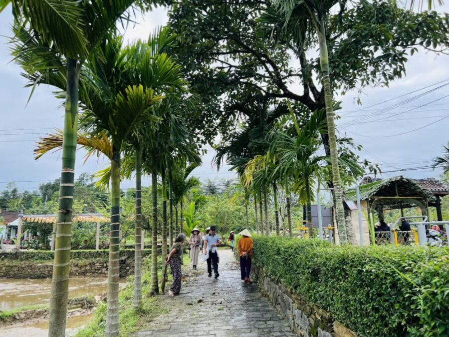People walking along a palm tree-lined path in Lộc Yên Ancient Village, Vietnam, showcasing a serene tropical atmosphere.