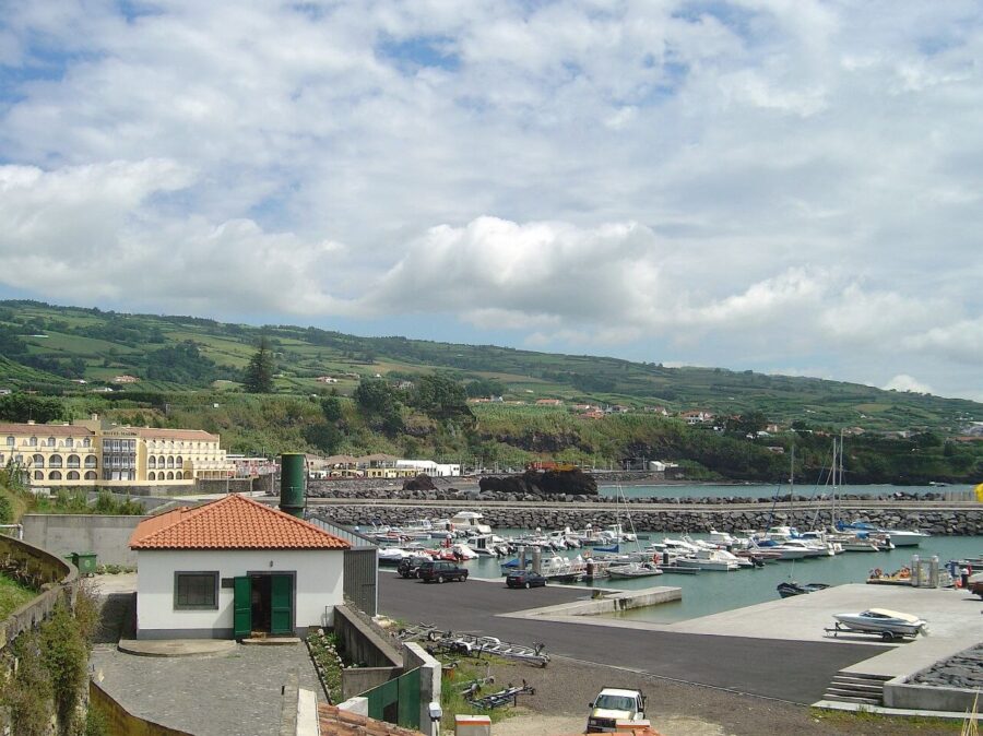 Coastal harbor with boats docked, surrounded by green hills and scattered buildings in Vila Franca do Campo