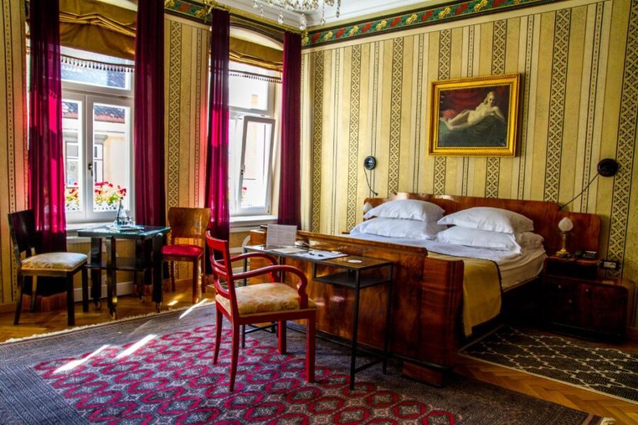 Interior of a bedroom at Vila Katharina in Brașov, showcasing a bed, chair, and table near a bright window.