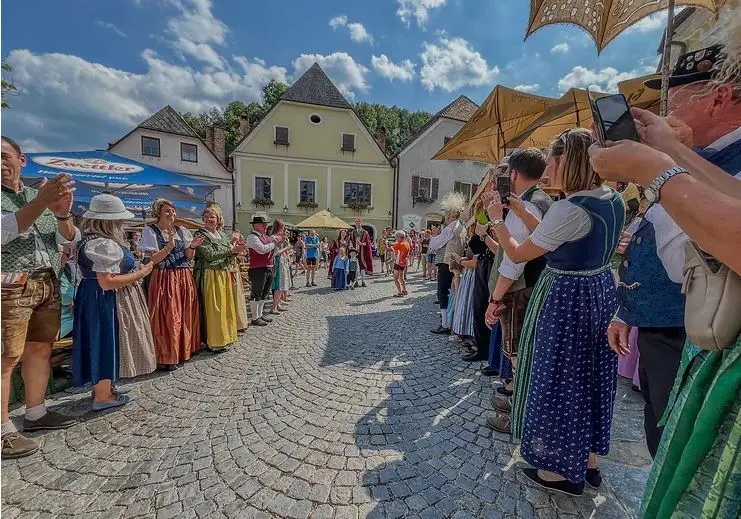 Traditional European village folk festival parade on cobblestone street with people in colorful costumes.