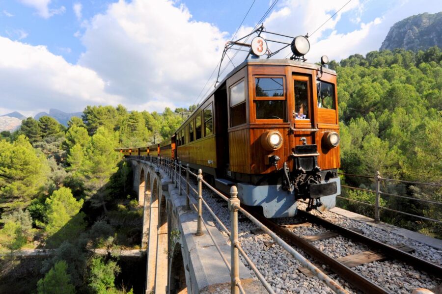 Vintage train crossing scenic viaduct with lush greenery and mountains.