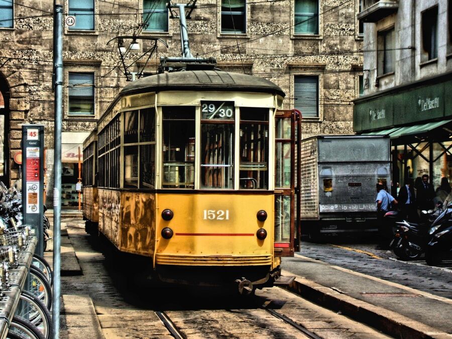 Vintage yellow tram in a vibrant urban setting with cobblestone street and historical architecture.