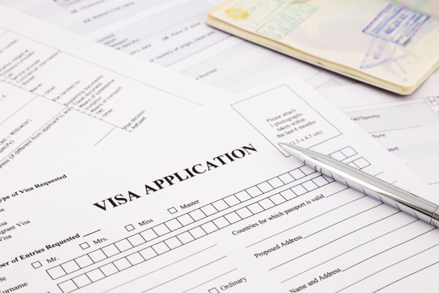 Pen placed on a visa application alongside a passport and travel documents on a desk
