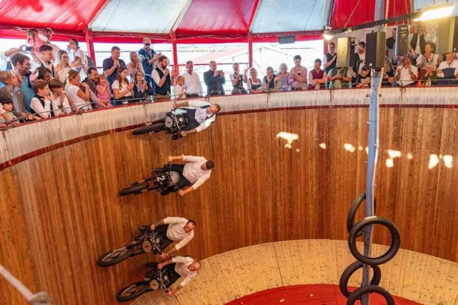 Wall of Death motorcycle stunt riders in wooden motodrome under carnival tent.