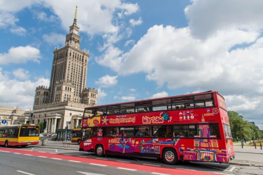 Warsaw City Sightseeing double-decker bus parked in front of a tall building, ready for tourists to explore the city.