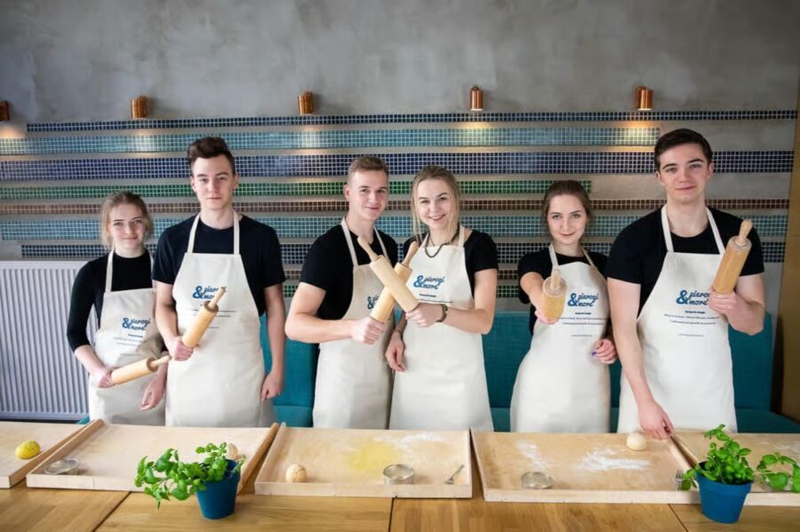 Young people in aprons gather around a table with dough at a Warsaw Polish dumpling cooking class with drinks.