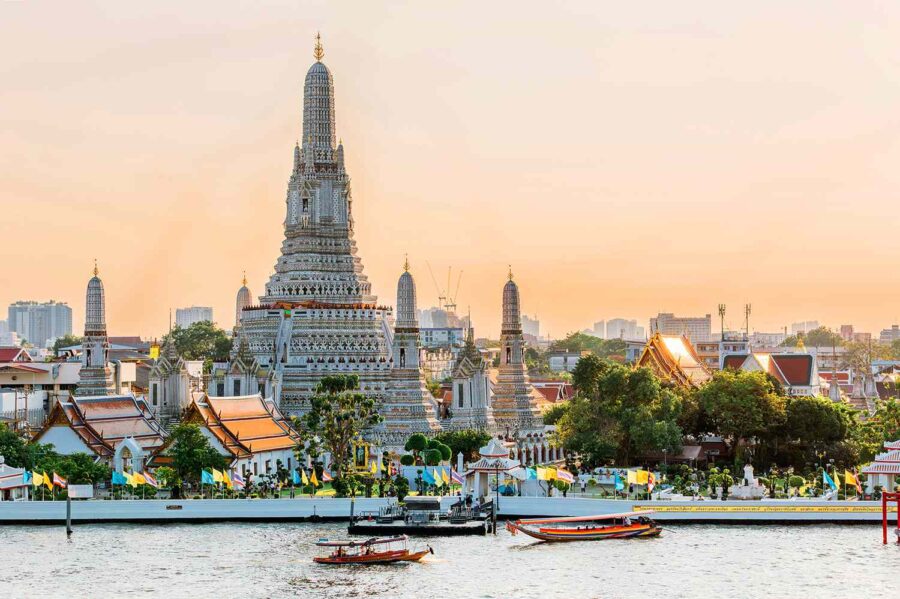 Silhouette of Wat Arun at sunset by Chao Phraya River, Bangkok, with long-tail boats.