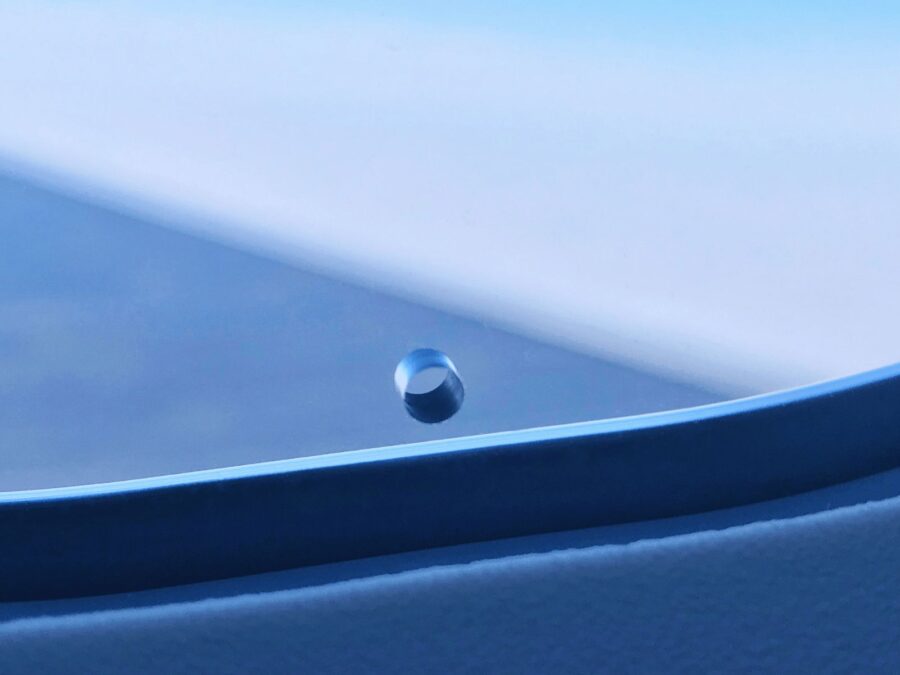 Airplane window with water droplet against sky, highlighting travel’s blend of nature and technology.
