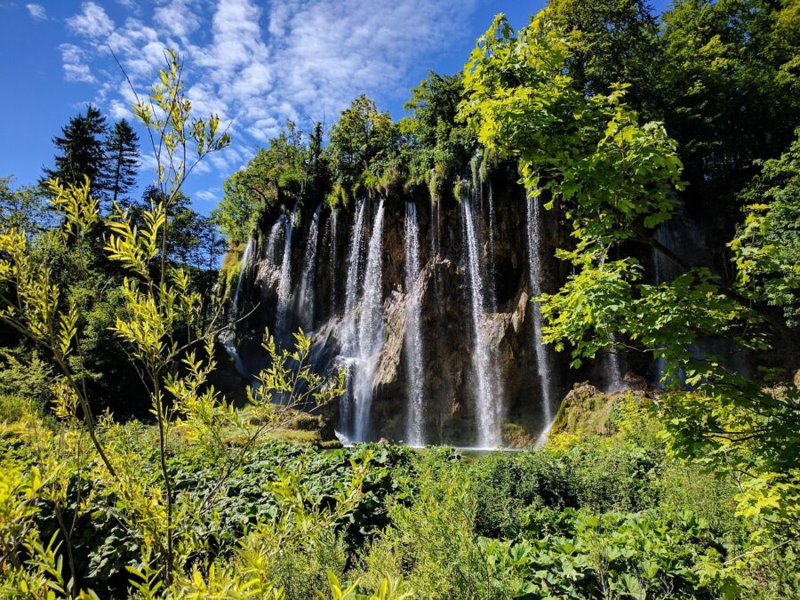 Picturesque waterfall in lush green forest with blue sky and moss-covered rocks.