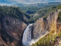 Majestic waterfall in a national park, surrounded by cliffs, trees, and vibrant nature.