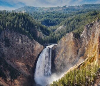 Majestic waterfall in a national park, surrounded by cliffs, trees, and vibrant nature.