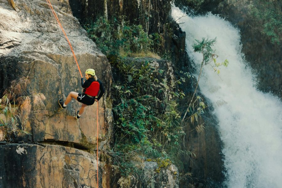 Climber rappels beside stunning waterfall with vibrant foliage, embracing thrilling adventure sports.