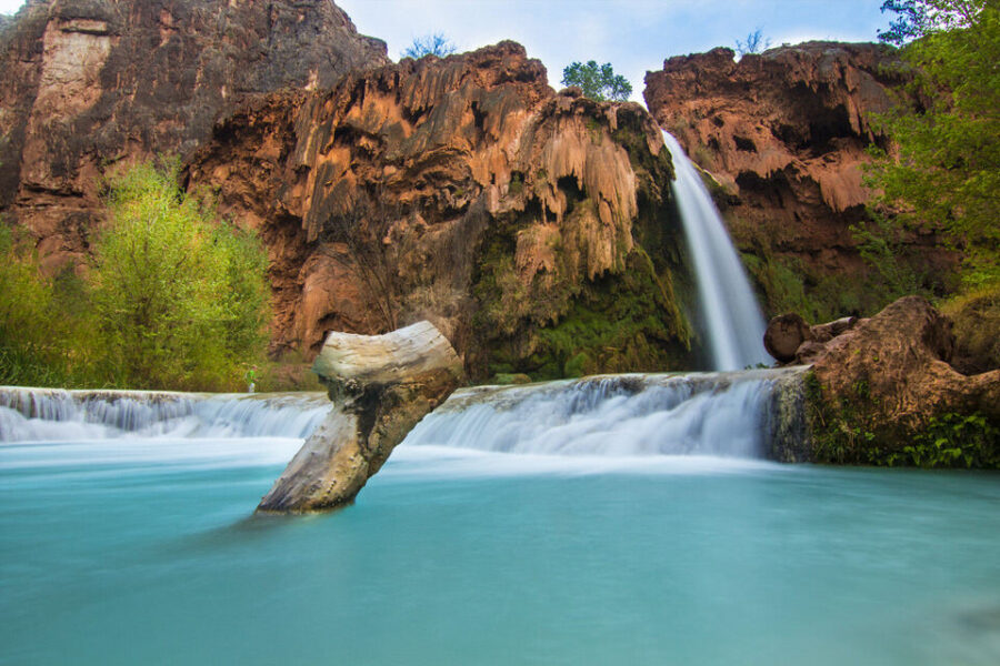 Majestic waterfall cascading over rugged cliffs into turquoise pool with vibrant, serene surroundings.