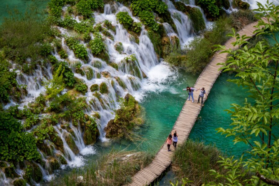 Waterfalls and turquoise waters surrounded by lush greenery and wooden walkways at Plitvice Lakes.