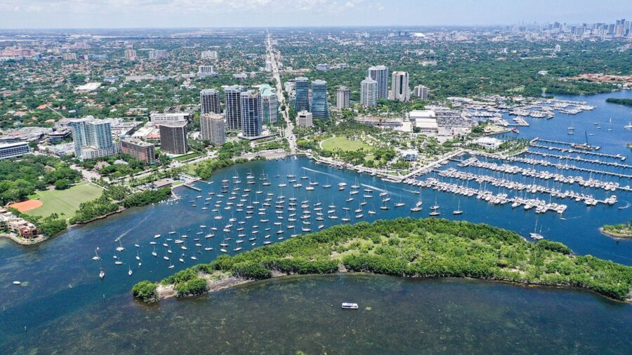 Aerial view of vibrant coastal city with marina, high-rise buildings, and lush greenery.